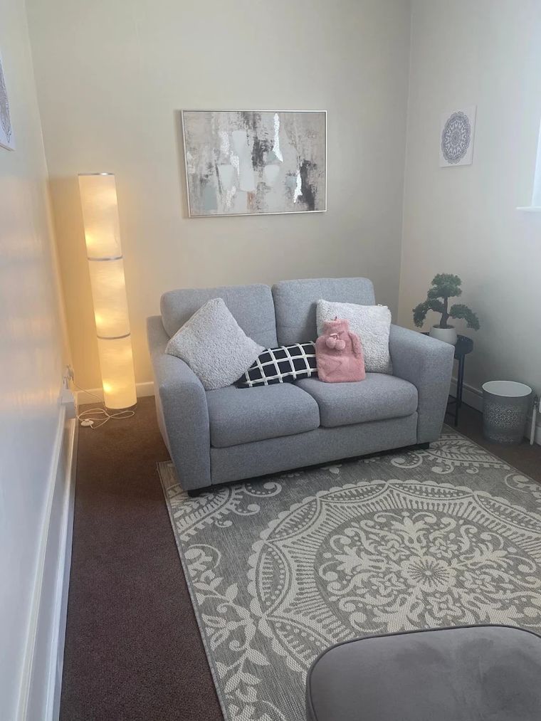 The counselling room: a soft grey sofa with cushions, warm lamp light and a patterned rug